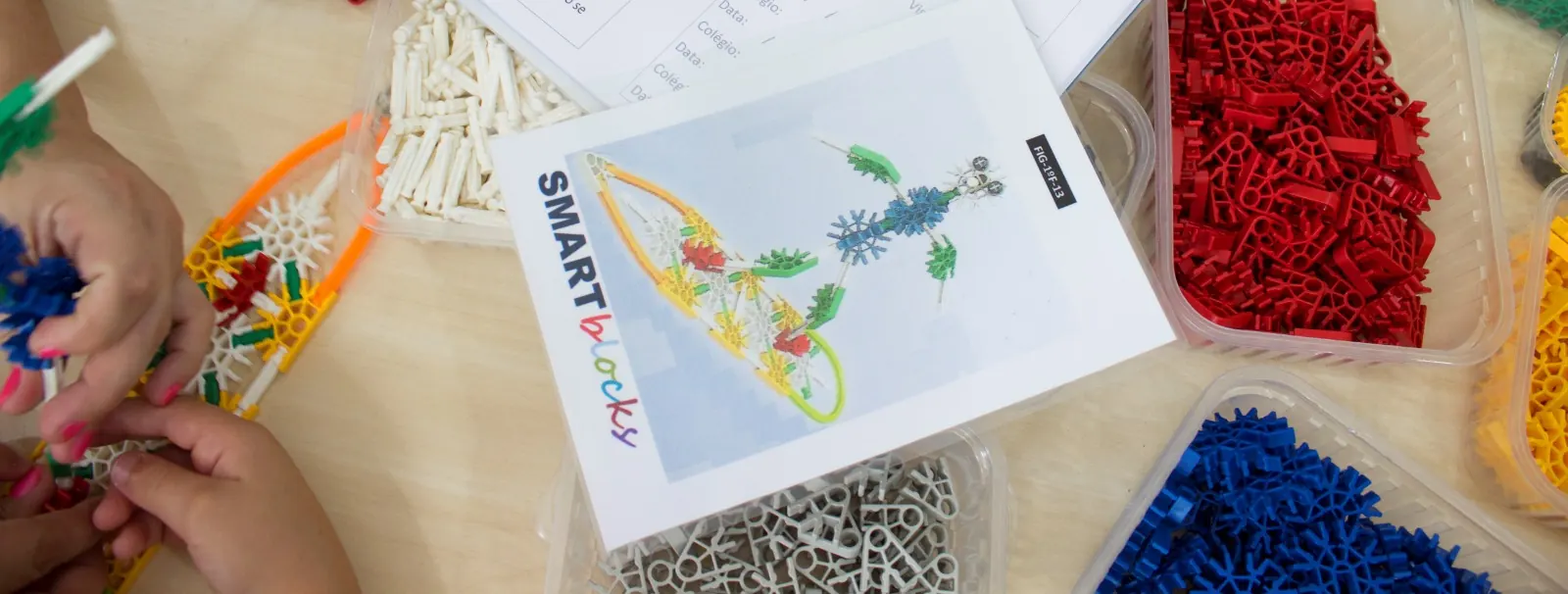 Ficha de montagem SMARTblocks sobre a mesa, com bandejas de peças K'NEX