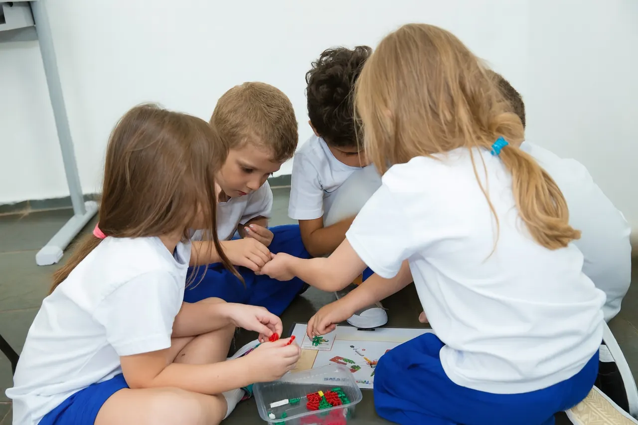 Alunos de uniforme montando um projeto com peças K'NEX no chão da sala de aula